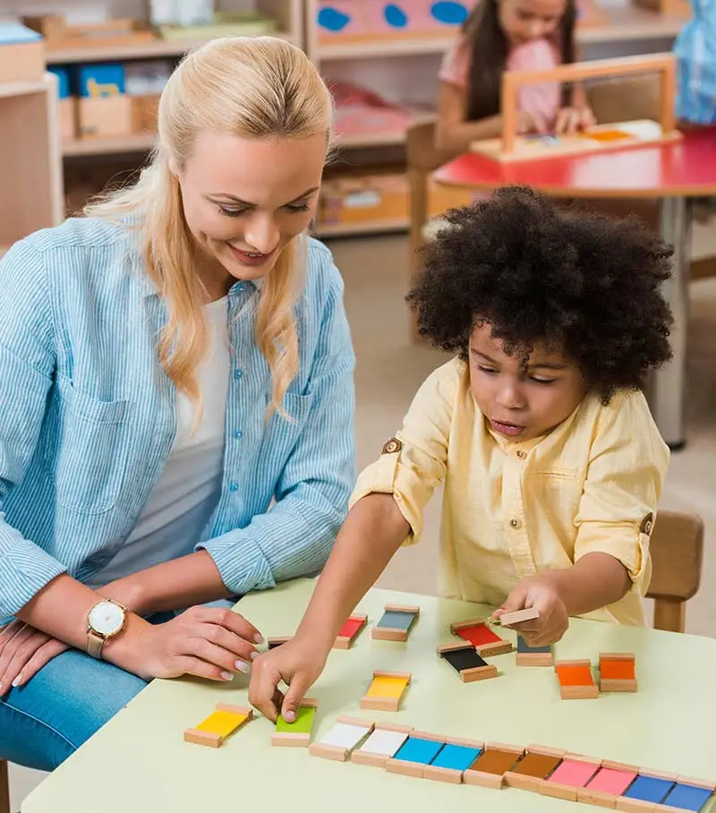 A childcare teacher working with a young boy at a table.