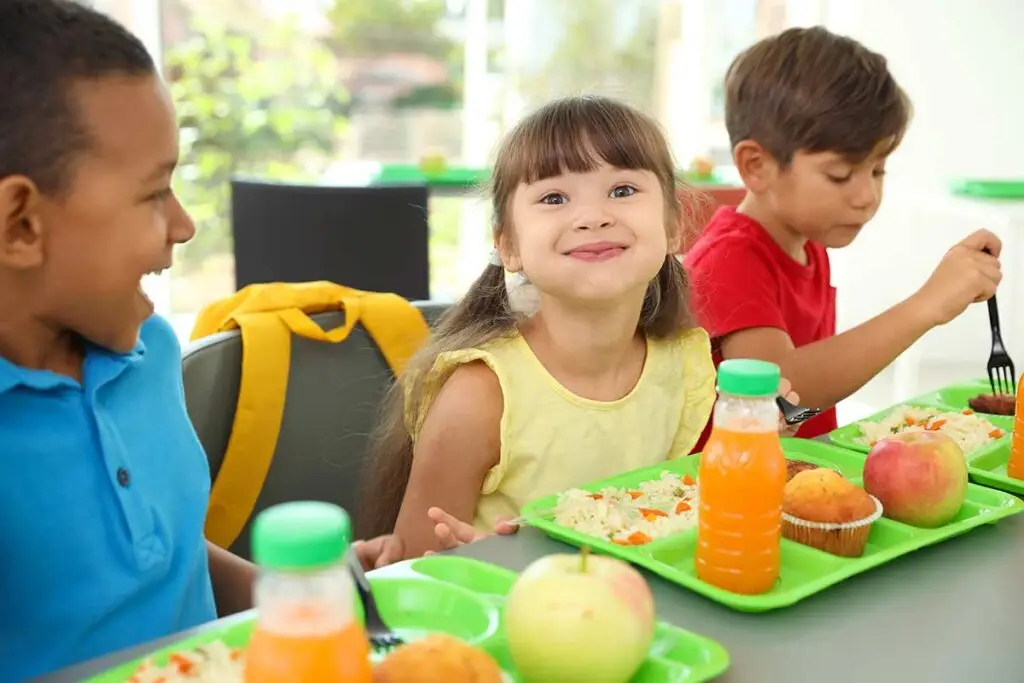 Children sitting at a lunch table eating healthy food.