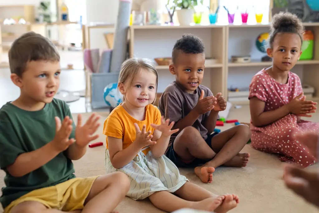 Young children sitting on the floor and clapping in a daycare classroom.