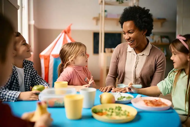 Children eating lunch with a teacher at daycare.