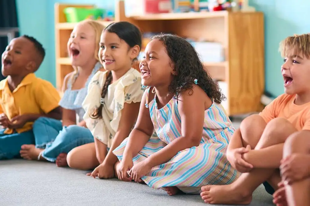 Happy children sitting in a line in a daycare classroom.